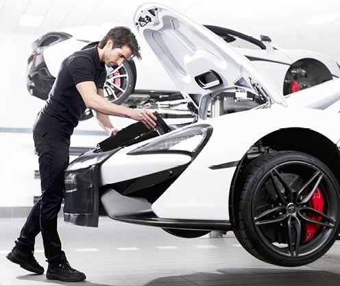 Service technician working on McLaren with hood open and car lifted
